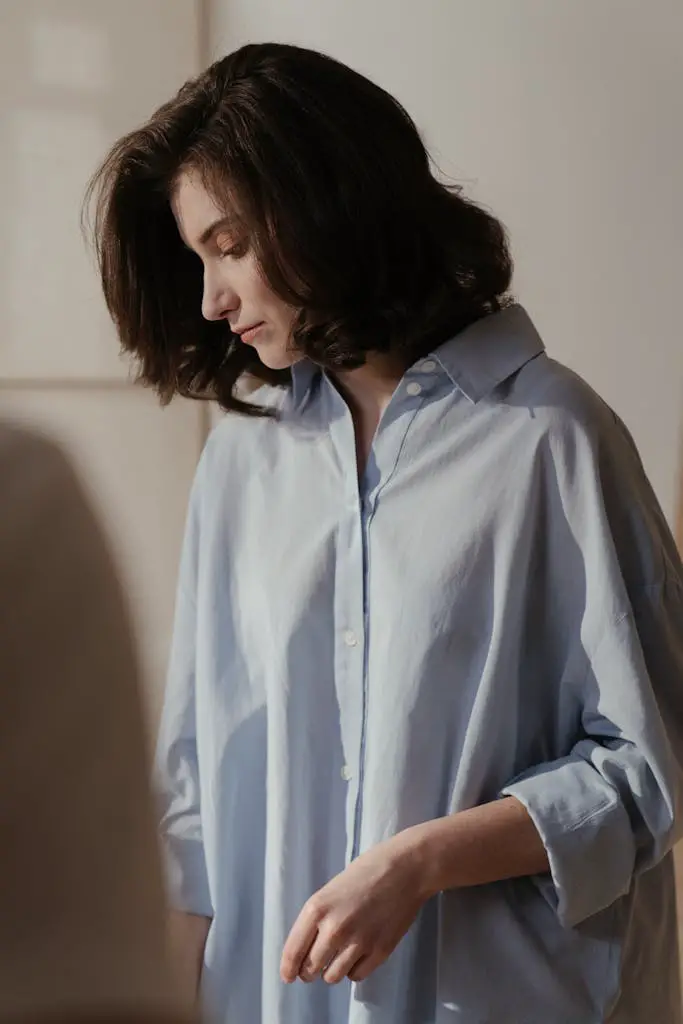 Thoughtful young woman in a blue shirt, captured in soft lighting.