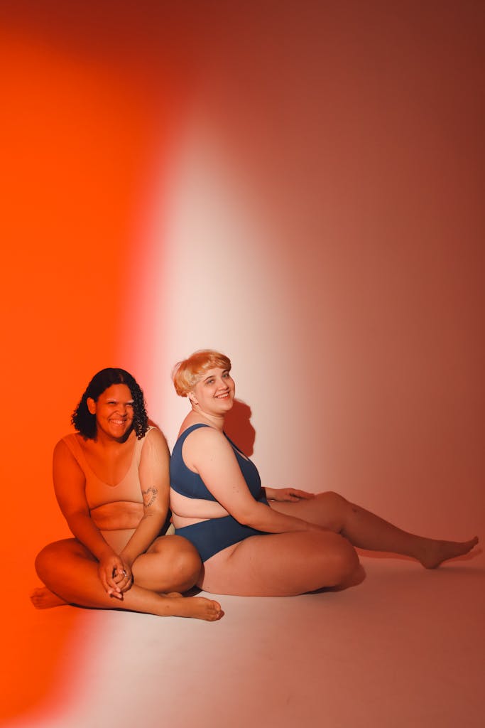 Two plus size women confidently pose in a vibrant studio setting.