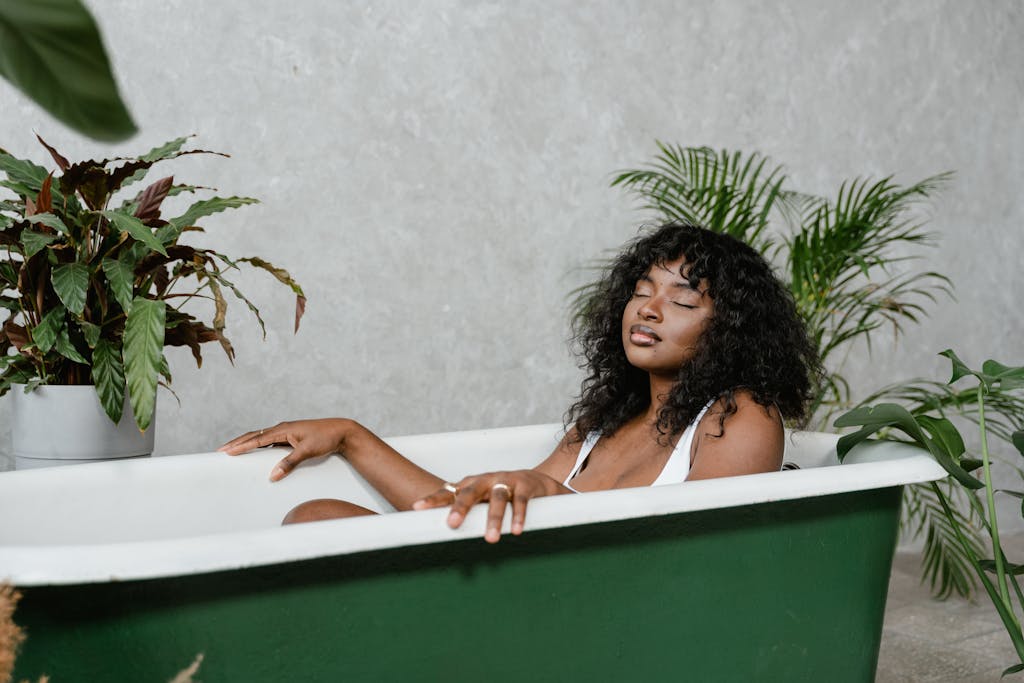 A serene woman with eyes closed, relaxing in a green bathtub surrounded by decorative plants.

plus size self care habits