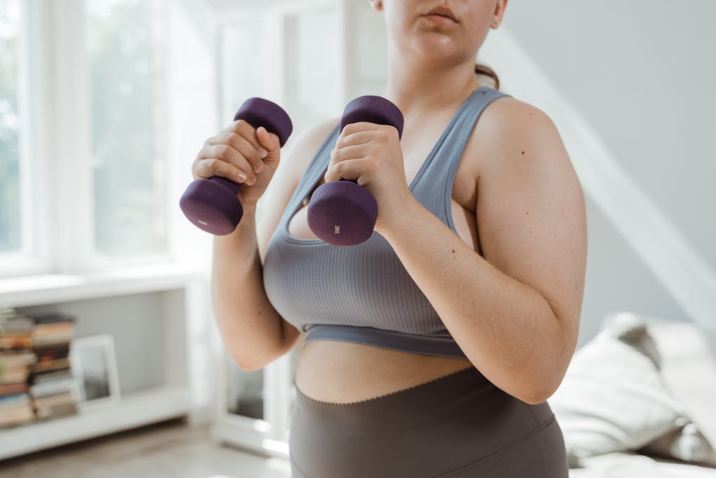 Plus size woman in activewear working out with dumbbells indoors, promoting body positivity. Plus size sports bra support