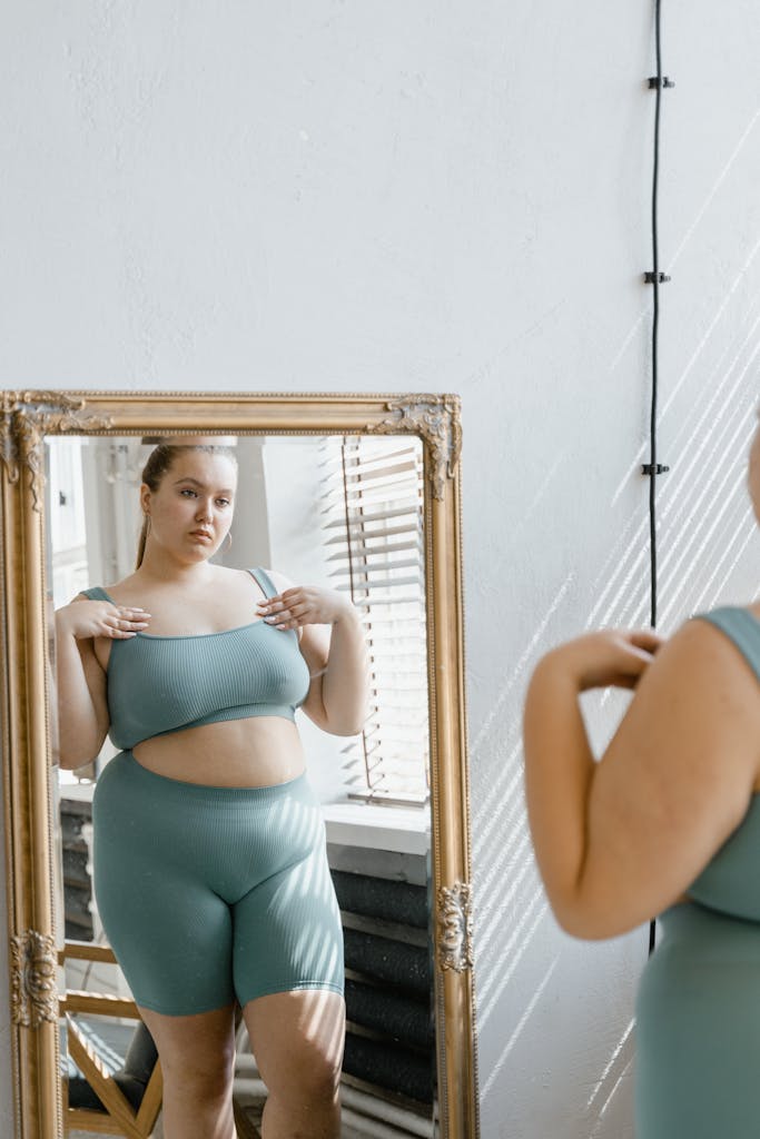 Confident plus size woman in sportswear looking at her reflection in a mirror indoors.

confidence in a thin obsessed world