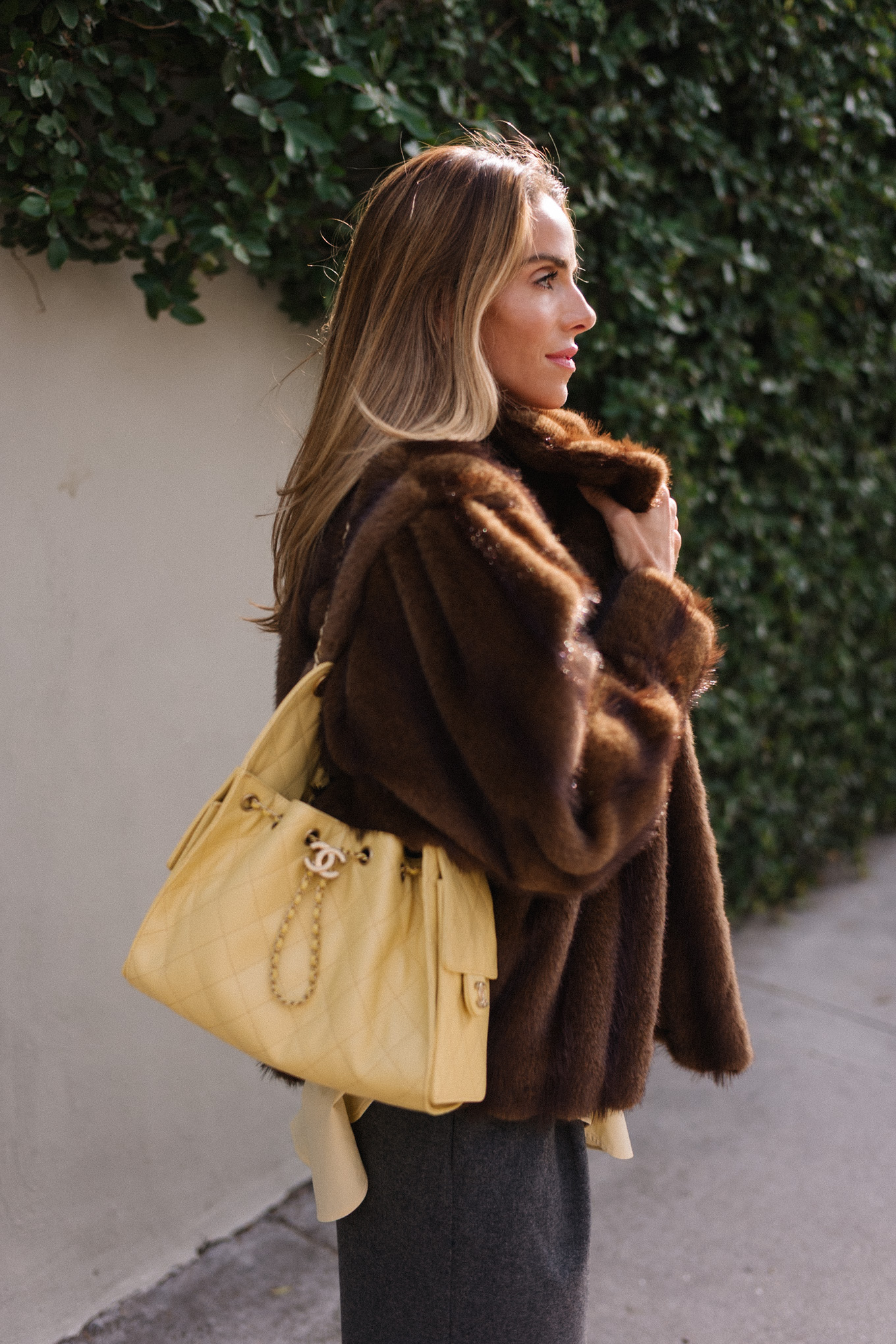 brown faux fur coat yellow button down shirt grey pants yellow tote red flats