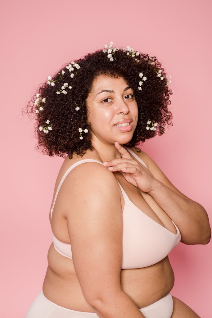 Content plus size African American female model in lingerie and small white flowers in black hair looking at camera on pink background
self-trust