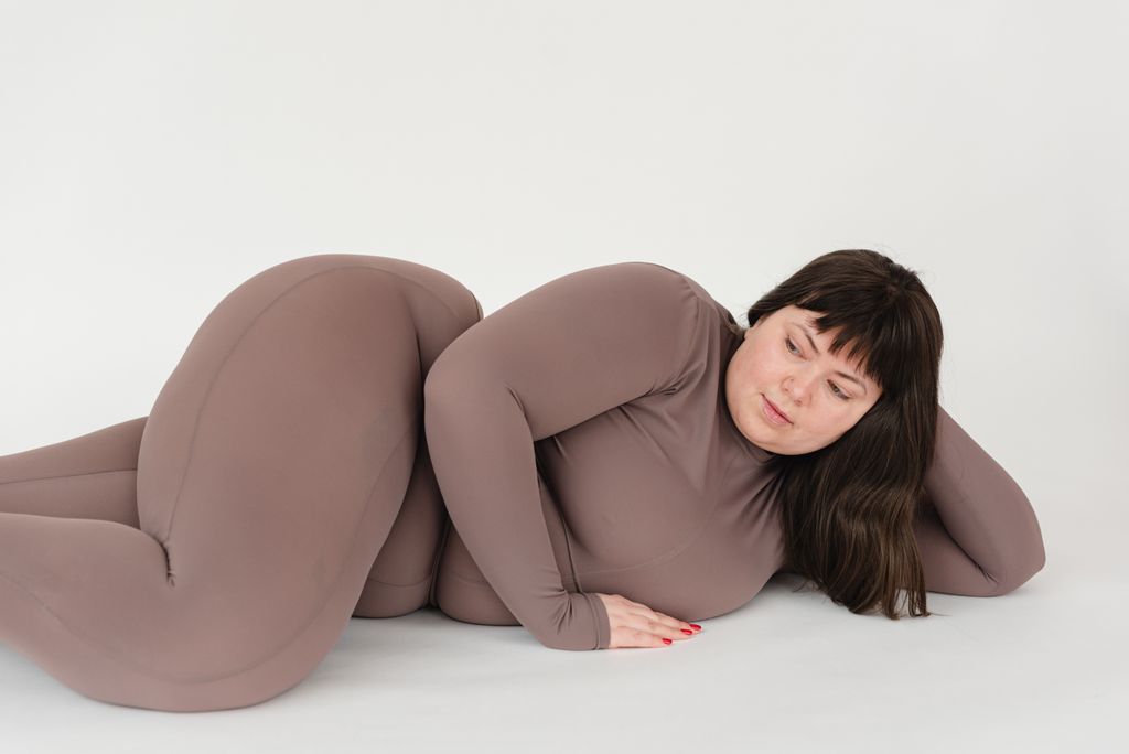 High angle of serious plus size female with long hair leaning on hand while lying against white background athletic wear
