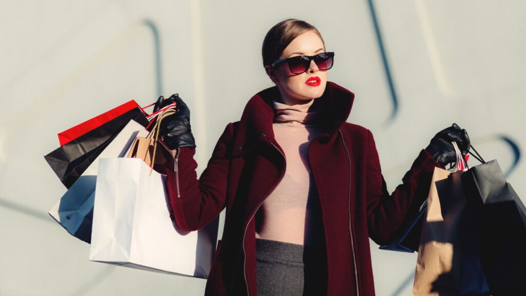Stylish young woman in sunglasses carrying shopping bags outdoors. Elegant fashion statement.